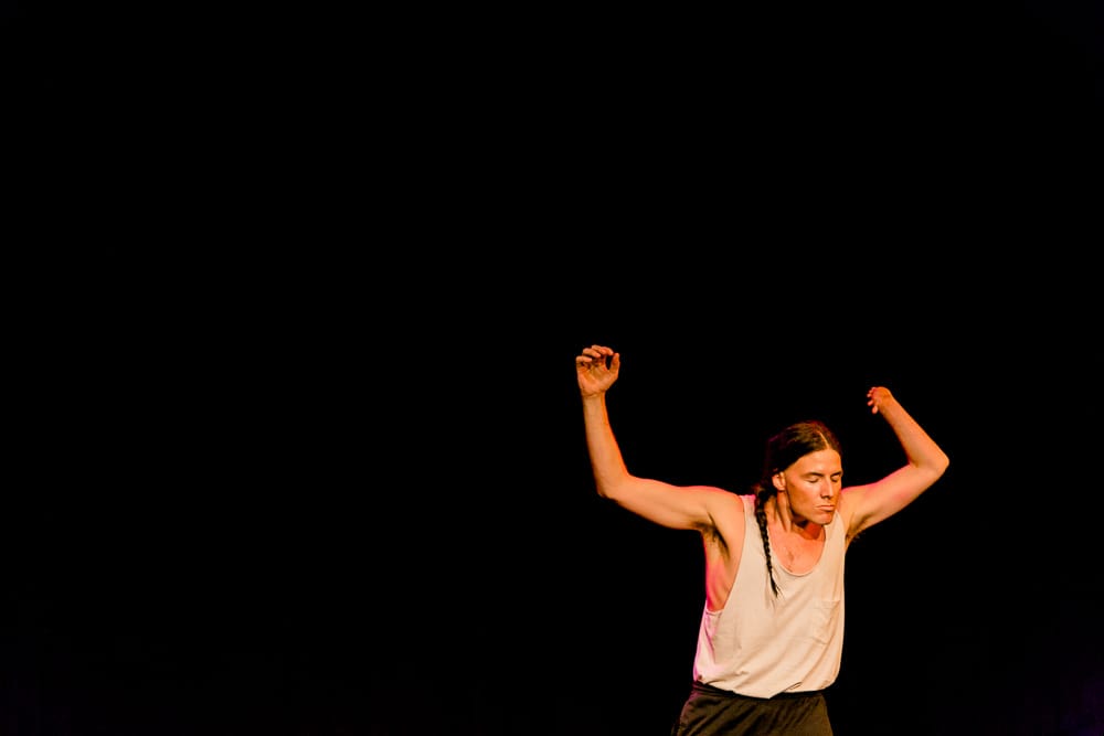 Brian performing with hands raised up in front of a black background.