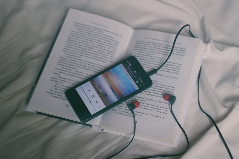 An iPhone and earphones sitting on an open book.