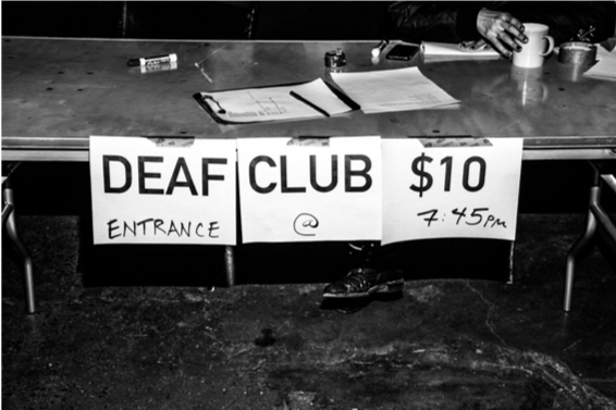 A sign hanging on a table reads "DEAF CLUB $10, Entrance @ 7:45pm