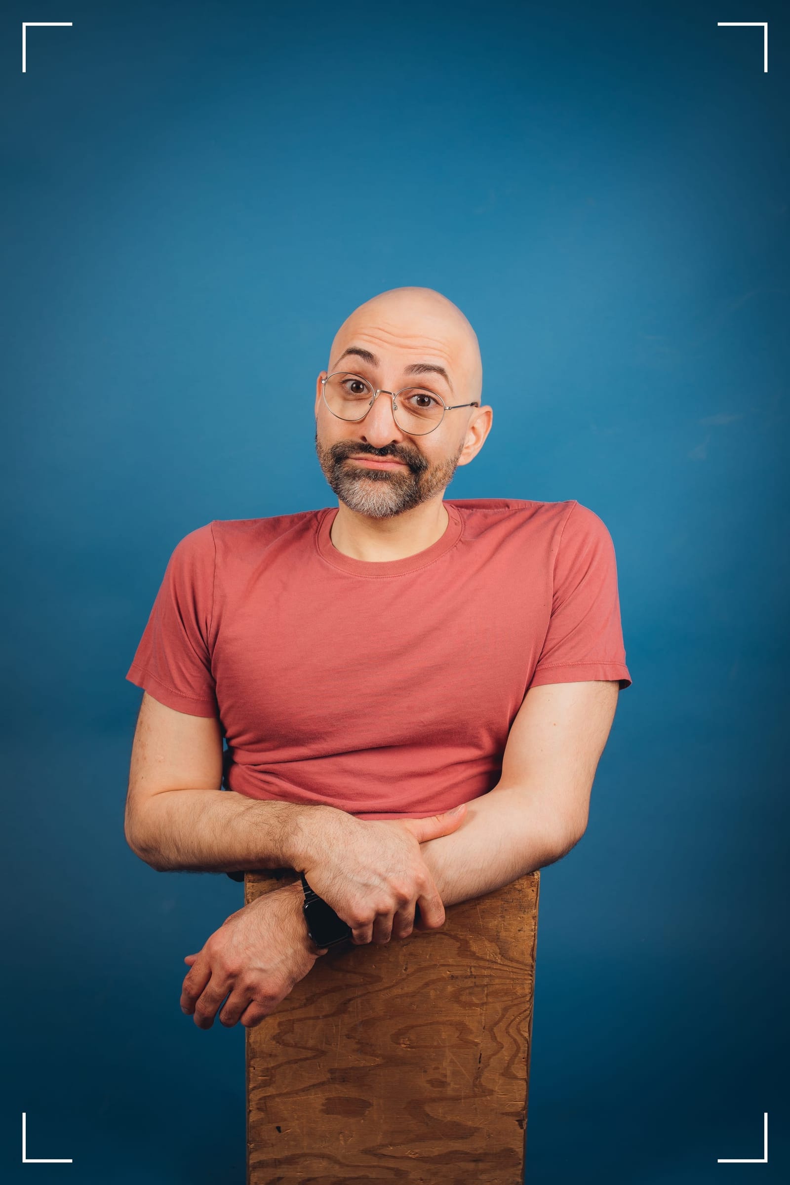 A headshot of Spencer West. Spencer is a disabled man, wearing round-framed glasses and a pink/orange t-shirt.