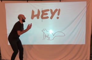 Connor stands in front of a screen with a projection image of a squirrel and "HEY!" in bold letters.
