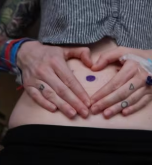 Alex holds her hands in a heart shape atop her stomach.
