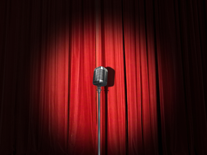 A lone microphone sitting in a spotlight on a stage with red curtains