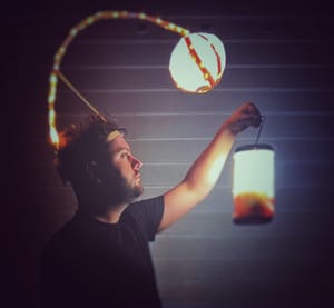 Landon in profile, holding a lantern with a light attached to a headband hanging above.